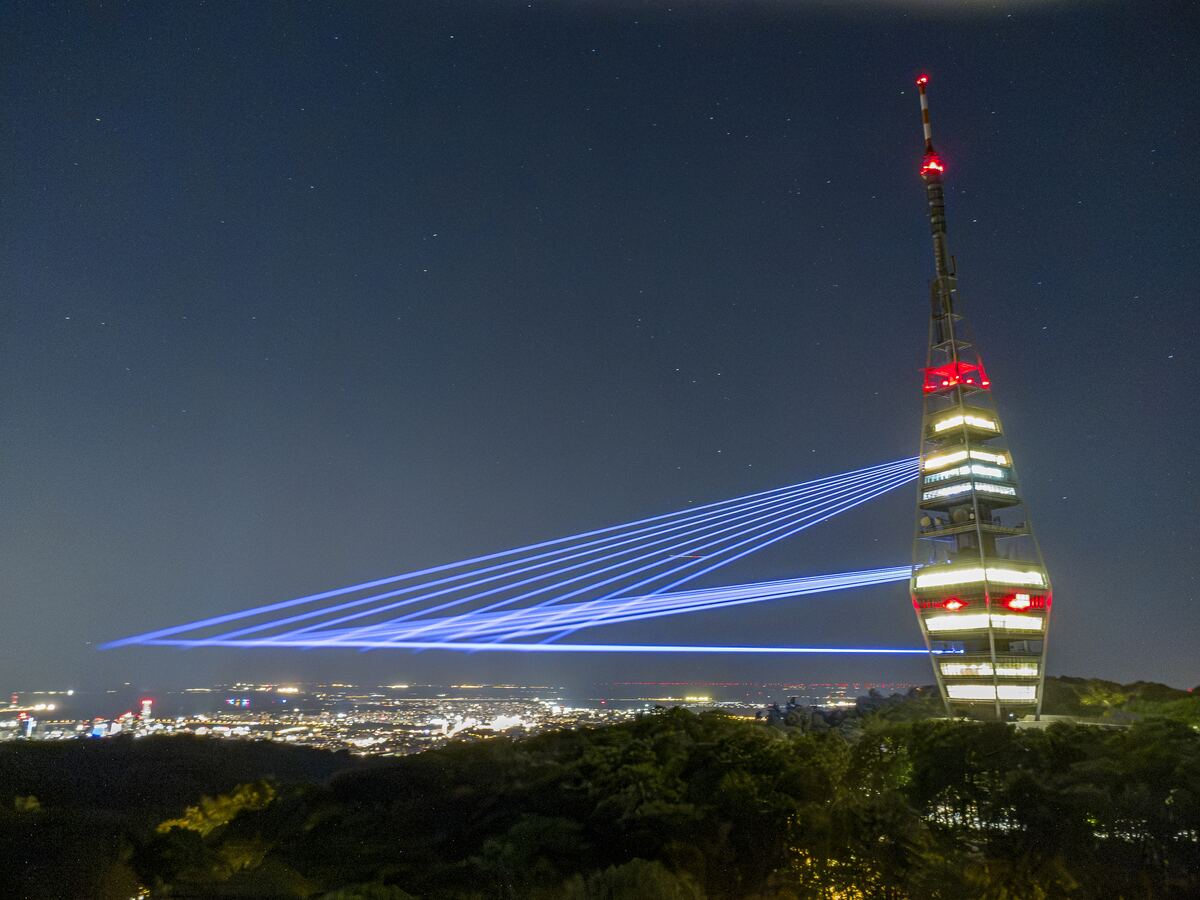 The Kamzík tower lit in white and red, a fan of blue beams reaching from it over the dark city.