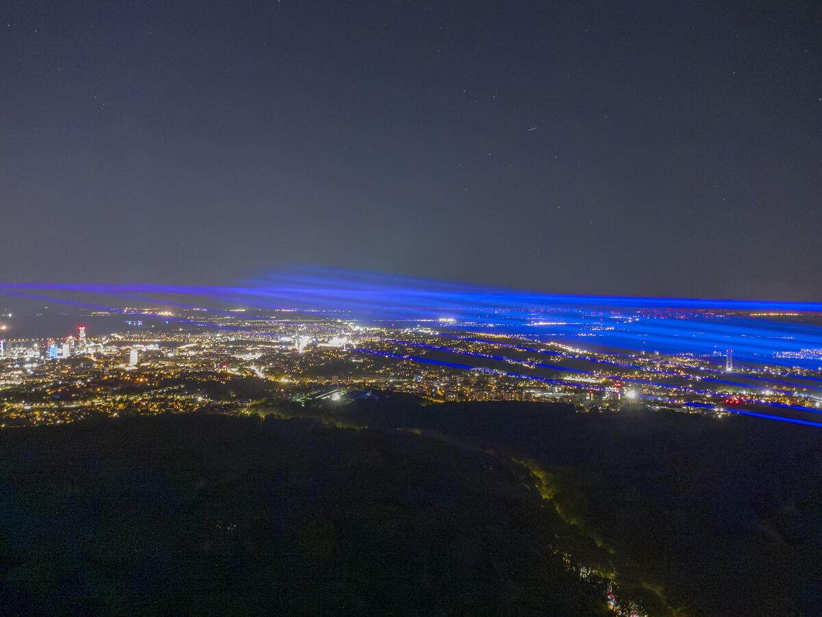 A band of blue laser light laid flat over the lights of Bratislava, the forest dark below.
