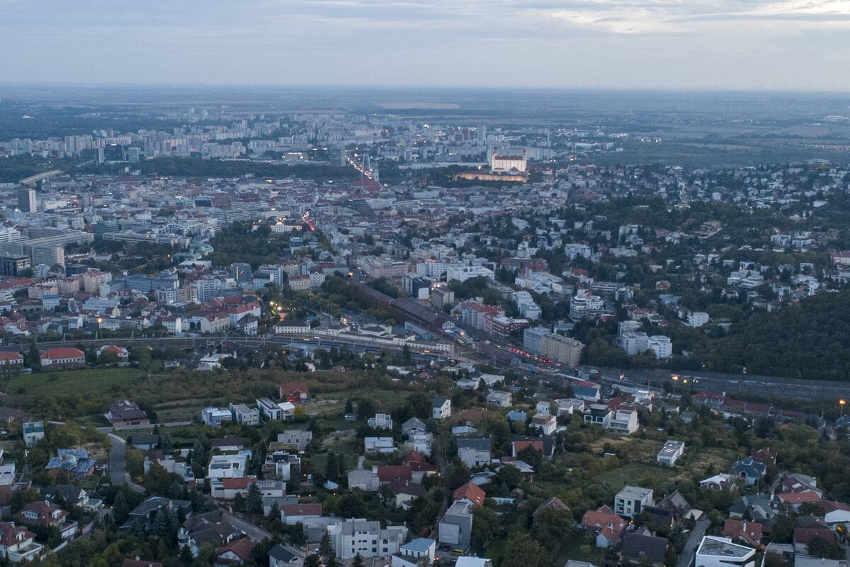 The city at blue hour, a railway line cutting through houses toward lit blocks on the horizon.